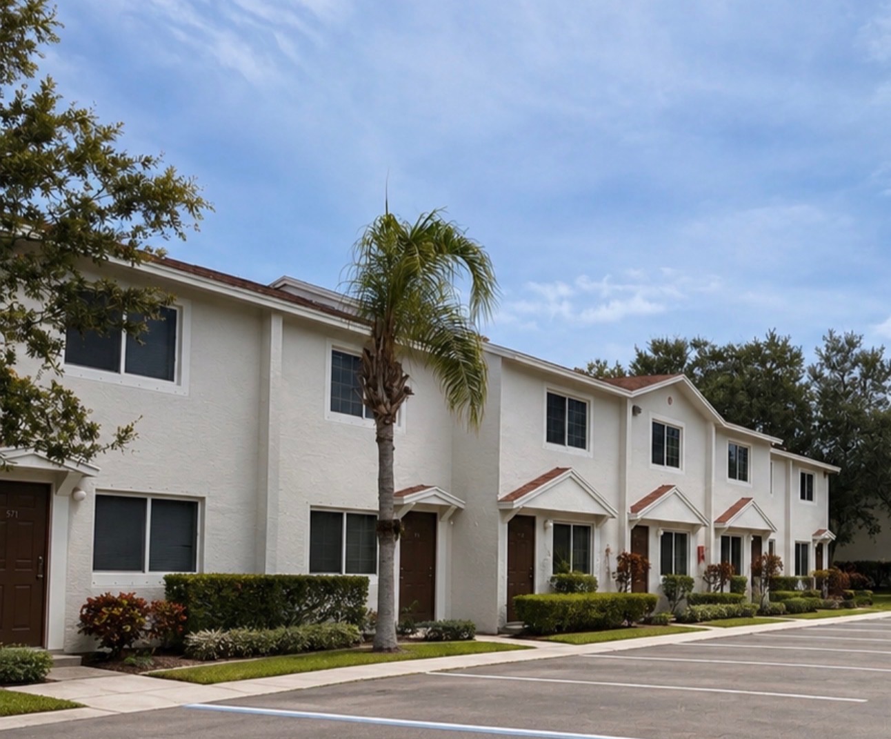 White two-story townhomes with palm trees and blue sky